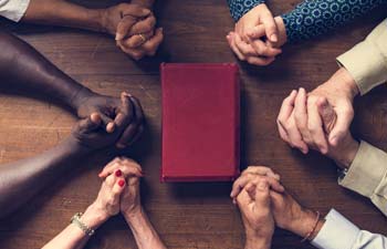 Hands praying around bible