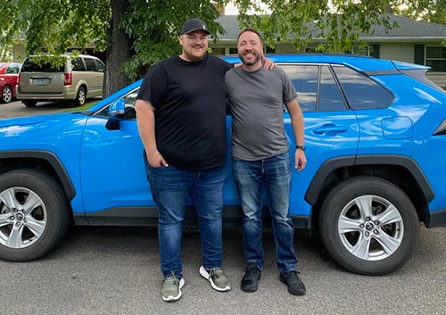 Two men smiling next to a car